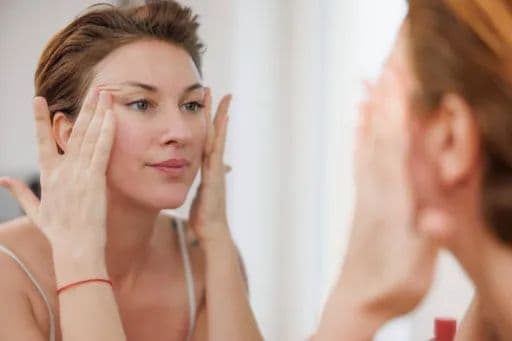 A woman observing the aging on her face as she stretches back her skin