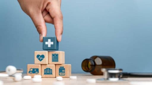 A hand placing 6 childrens blocks with medical insignia into a pyramid while medications are surrounding them.