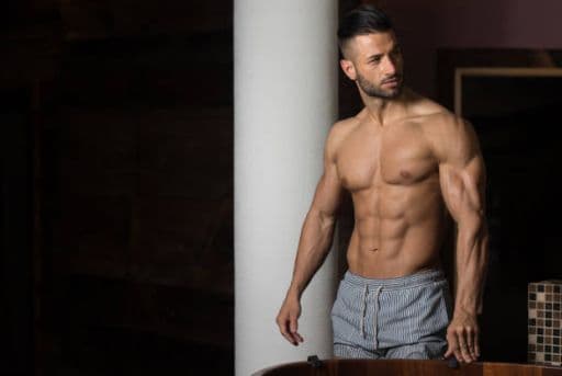 A man looking around his room with his shirt off, revealing ripped abs