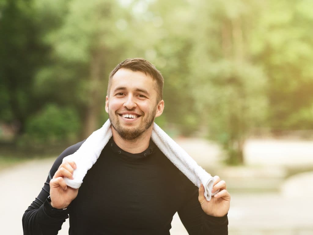 A man wearing a towel around his neck while smiling into the camera.