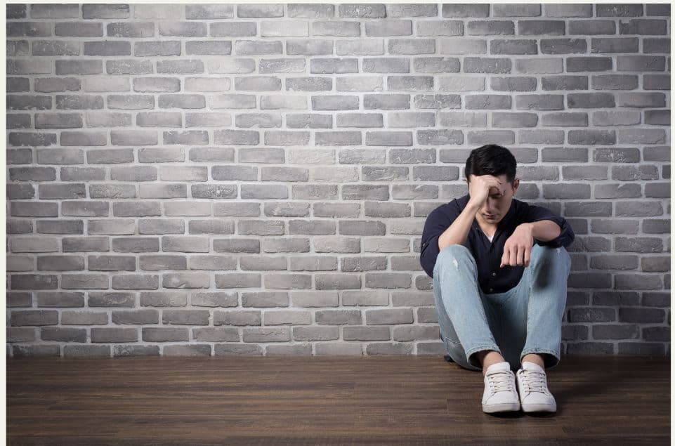 A depressed man sitting alongside a wall with his hand on his head. Clearly needs TRT.