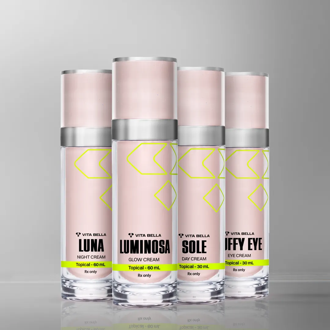 Four Vita Bella skincare products for women are displayed on a reflective surface with a light gray background. From left to right: a container labeled "Luna Night Cream" (topical, 60 mL), a container labeled "Luminosa Glow Cream" (topical, 60 mL), a container labeled "Sole Day Cream" (topical, 30 mL), and a container labeled "Jiffy Eye Cream" (topical, 30 mL). Each container has a pink label with yellow accents and "Rx only" markings.