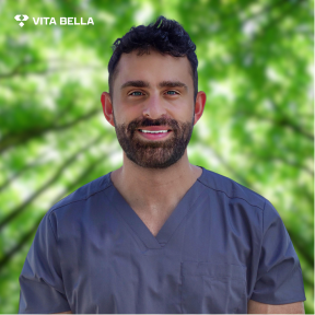 Dr. Daniel Bryan, Chief Medical Advisor at Vita Bella, wearing a blue scrub top, with a green background and text identifying his role as an Anesthesiologist and Hormone & Peptide Specialist.