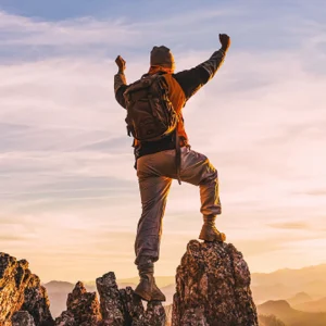 A person standing on a rock with arms raised in triumph against a sunset, symbolizing weight loss success and achievement